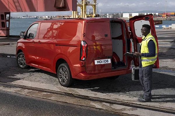 Heckansicht des roten Ford Transit Custom mit geöffneter Hecktür am Containerhafen, Mann in Warnweste steht mit Tablet an der Tür.