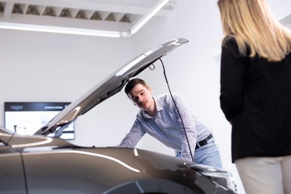 Serviceberater erklärt einer Kundin den aktuellen Fahrzeugzustand vor der geöffneten Motorhaube ihres Fahrzeugs in der Direktannahme im Autohaus Hempel.